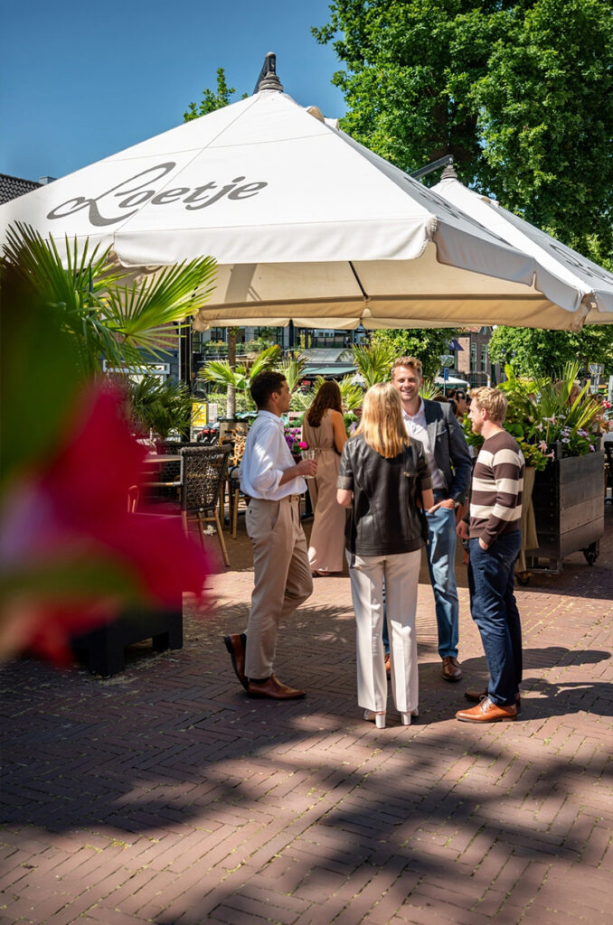 Gasten op het zonnige terras van Loetje Bergen onder een grote Loetje-parasol.