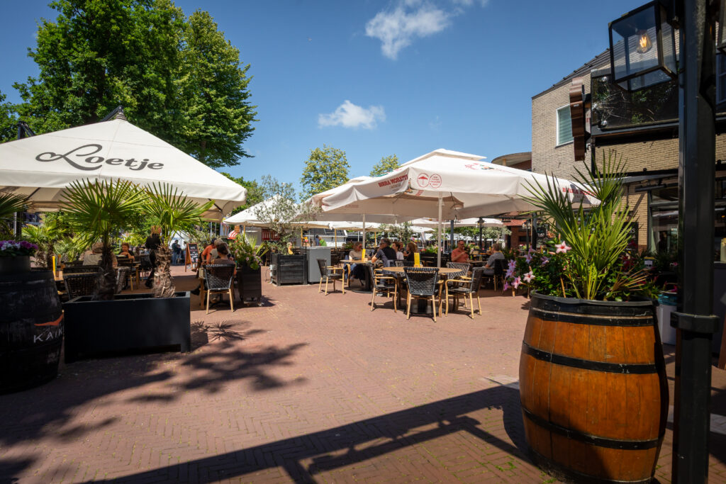 Zonnig terras van Loetje Bergen met gasten onder grote parasols.