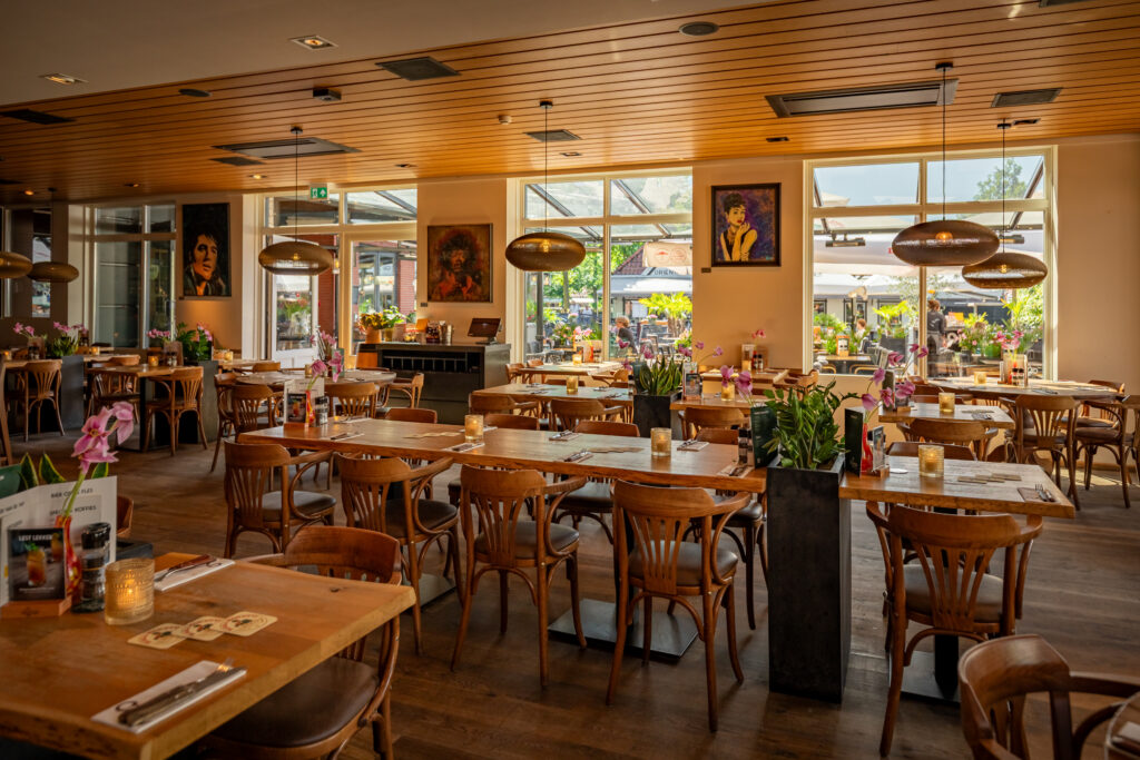 Ruim interieur van Loetje Bergen met gedekte houten tafels en uitzicht op het terras.