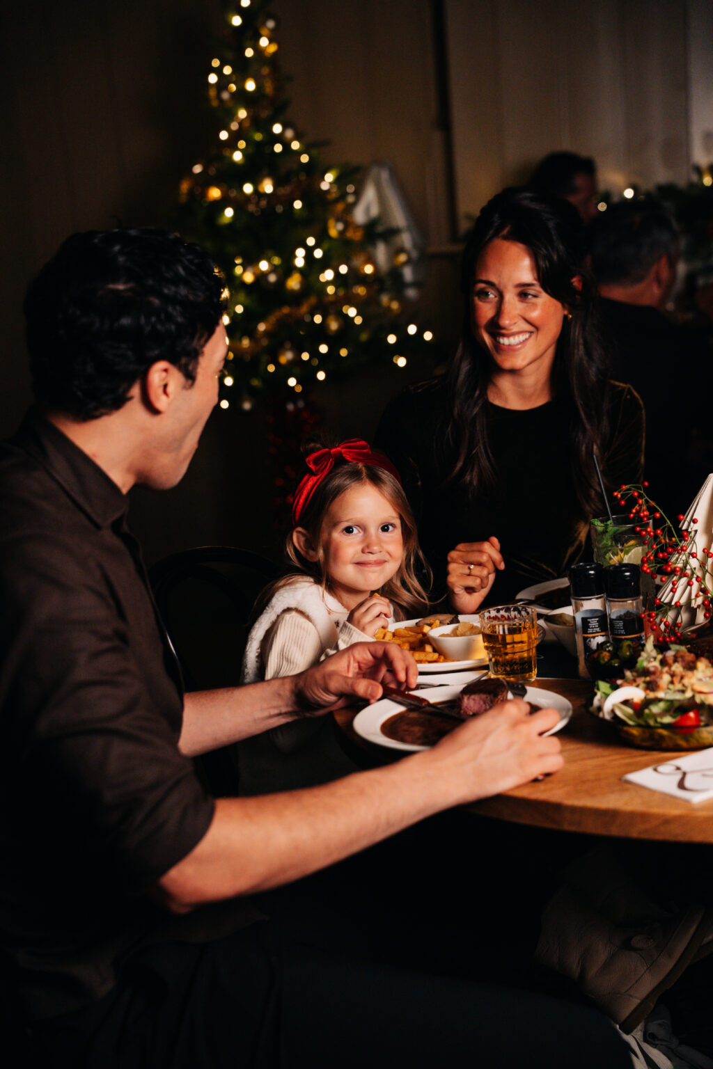 Gezin geniet samen van een kerstdiner bij Loetje, met een versierde kerstboom op de achtergrond.